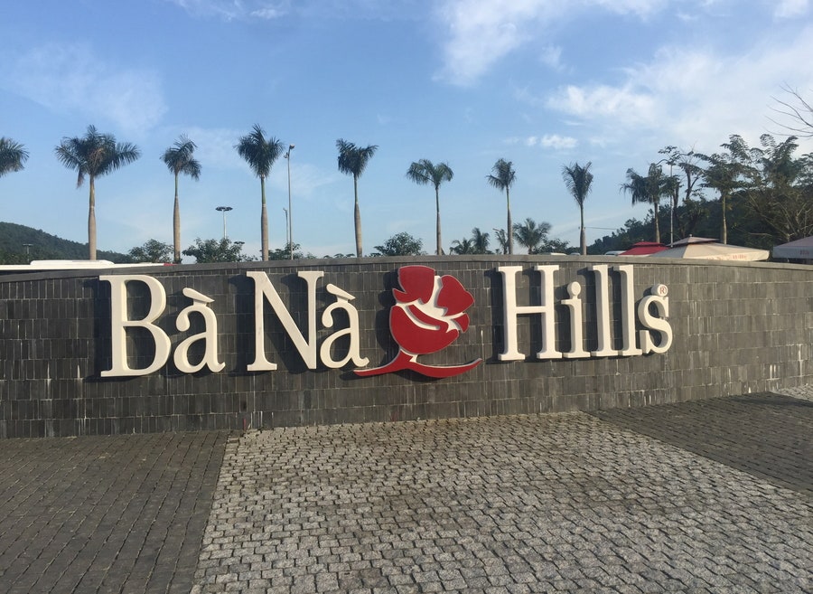 야자수와 광장 입구 화단 뒤편으로 'Bà Nà Hills' 브랜드 영문 입체 조형물이 설치된 입구 전경