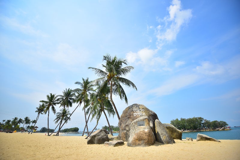 야자수들이 줄지어 선 백사장 해변과 'SILOSO BEACH'가 새겨진 큰 바위 포토존, 잔잔한 바다가 보입니다.[cite: 6]