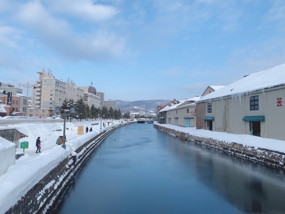 눈 쌓인 산책로와 붉은 벽돌 창고 건물 사이로 잔잔하게 흐르는 겨울 오타루 운하