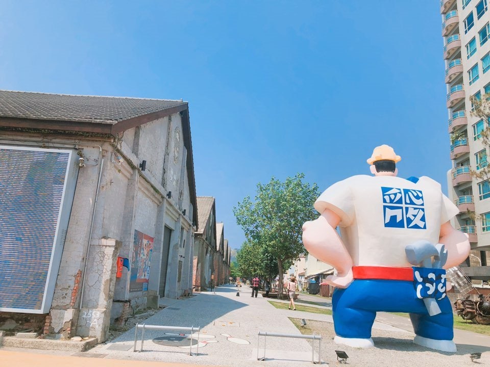 부두 옛 창고 건물 사이 야외 광장에 설치된 대형 노동자 캐릭터 조형물과 푸른 하늘