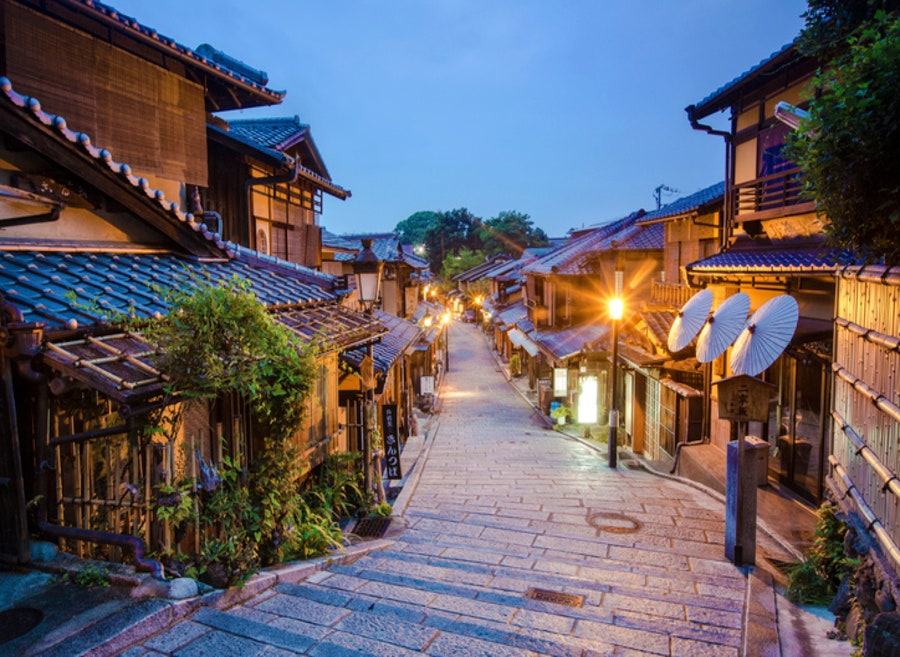 돌계단 길을 따라 전통 가옥과 지붕, 켜진 가로등 및 우산 장식이 어우러진 교토 니넨자카/산넨자카 거리 풍경